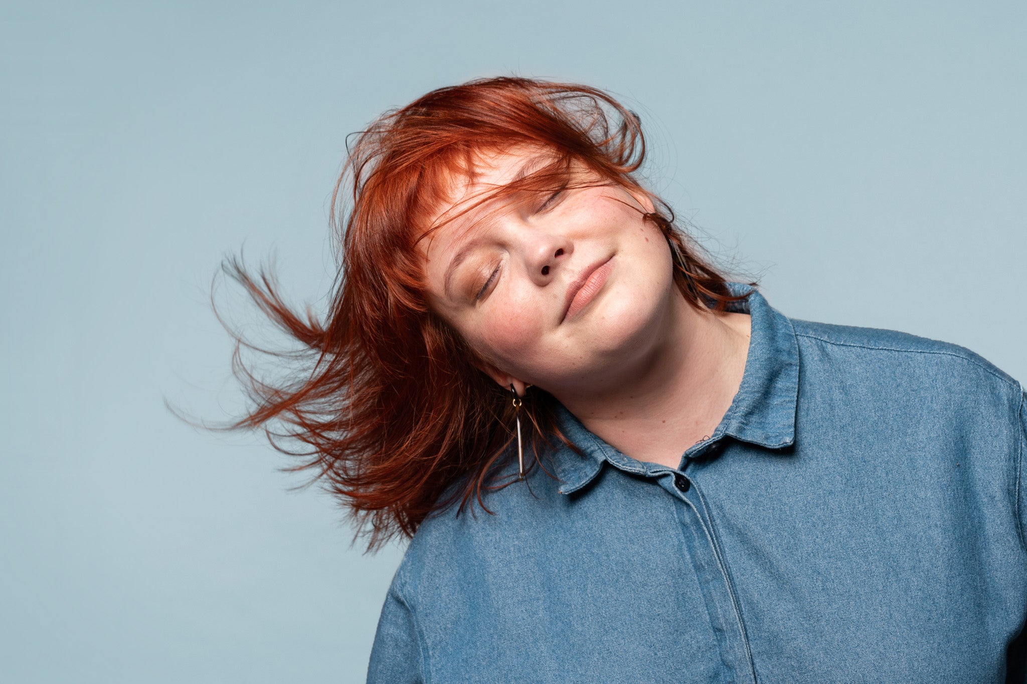 A red headed woman with her hair blowing in the wind. She is eco-chic.